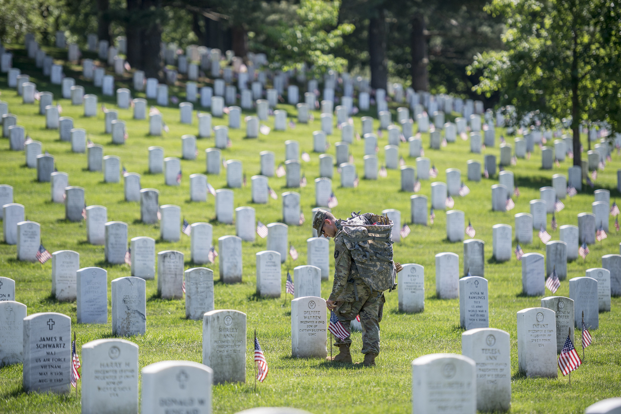 after_funeral A uniformed soldier places American flags in front of gravesites at Arlington National Cemetery